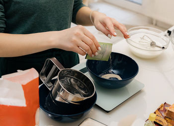 A young girl pours dry yeast into a bowl on the table.