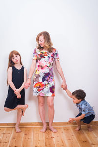 Full length of family standing on hardwood floor against wall