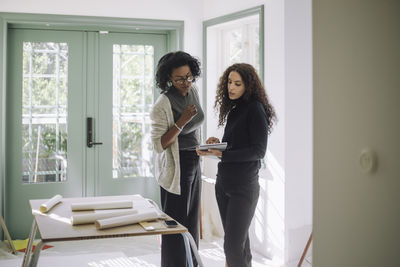 Architect discussing with female client over digital tablet while standing at under construction apartment