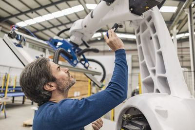 Engineer examining robotic arm with flashlight in industry