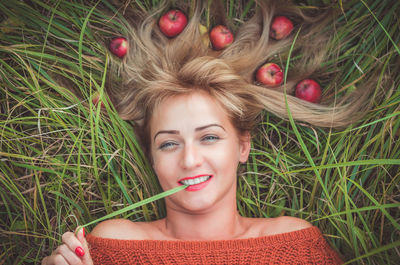 Directly above portrait of happy woman lying with apples on grassy field
