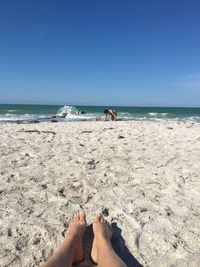 Low section of woman sitting on sand while girl kneeling on shore