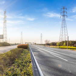 Road by electricity pylon against sky