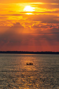 Sunrise on the amazon river in brazil, a small boat sails in the reflection of the sunlight