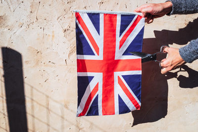 Cropped hand of person cutting british flag against wall