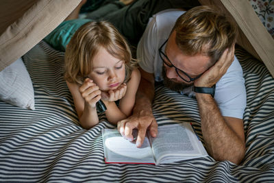 Father and son playing and reading in a kid tent at home.