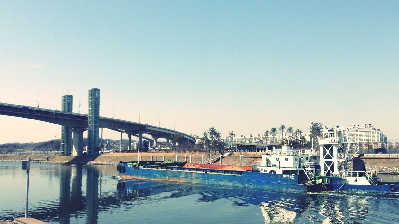 built structure, architecture, bridge - man made structure, connection, water, clear sky, copy space, transportation, river, engineering, bridge, waterfront, building exterior, city, suspension bridge, outdoors, nautical vessel, no people, mode of transport, blue