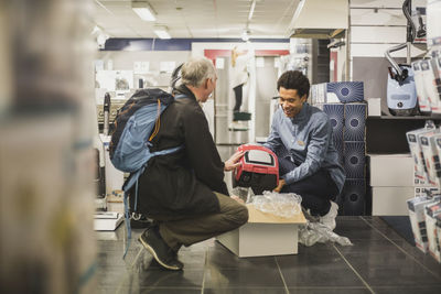 Smiling young salesman showing appliance to male customer in store