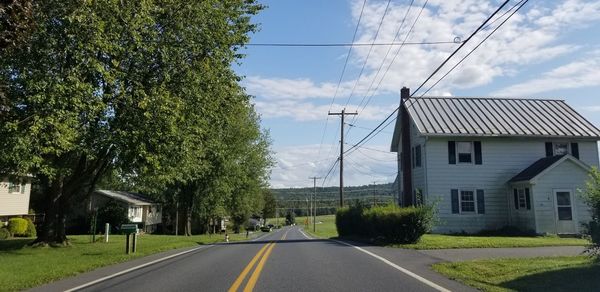 Road by trees and buildings against sky