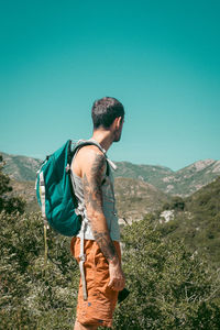 Young man looking at mountain range against clear sky