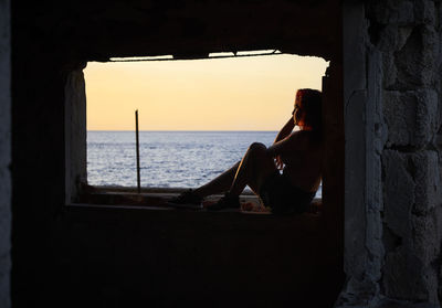 Full length of woman sitting by window at sea