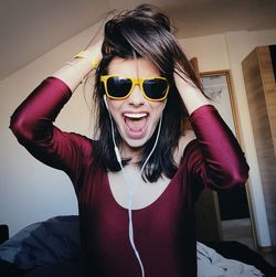 Portrait of young woman shouting while listening music while wearing sunglasses at home