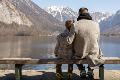 Father and son sitting together outdoors on the bench and enjoying mountains, snow