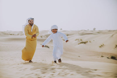 Full length of friends enjoying on sand against sky