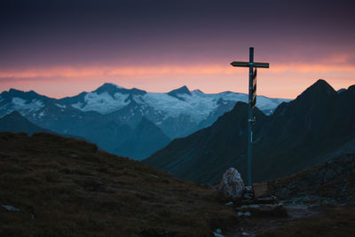 Cross on mountains against sky during sunset