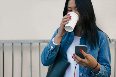 Teenage girl drinking coffee while using mobile phone