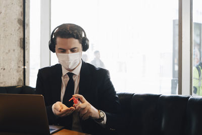 Businessman with hand sanitizer sitting at cafe working with laptop