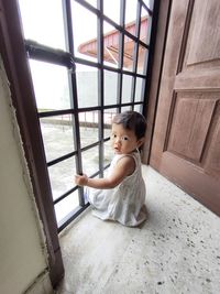 Portrait of cute girl sitting against window at home