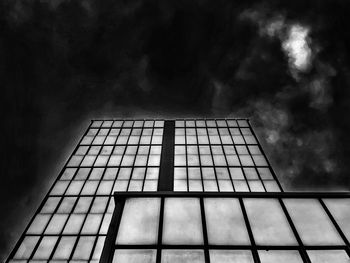 Low angle view of glass building against cloudy sky