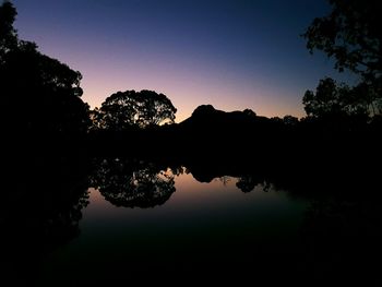 Reflection of silhouette trees in lake against sky at sunset