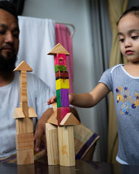 Father looking at girl playing with toy blocks