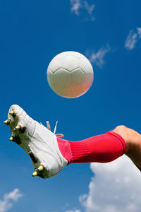Low section of soccer player kicking ball against blue sky
