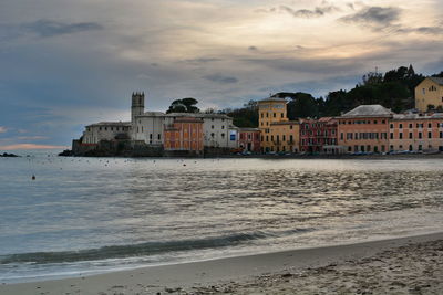 Buildings by sea against sky at sunset