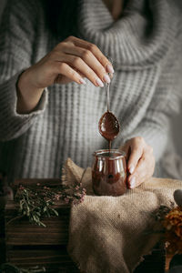 Midsection of woman holding spoon over chocolate jar on table