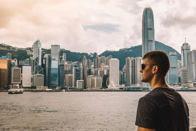 Handsome young man standing by harbor against buildings in city