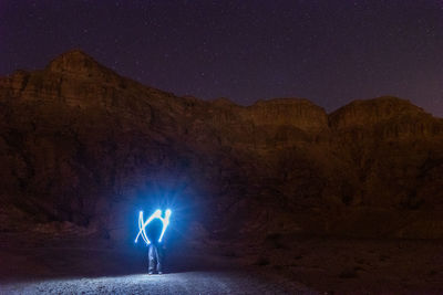 Man standing on illuminated rock against sky at night