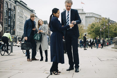Male and female entrepreneurs using smart phone while standing on street in city