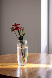 A bouquet in a transparent vase on a wooden table in the rays of the sun.