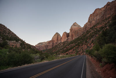 Road leading towards mountains against clear sky