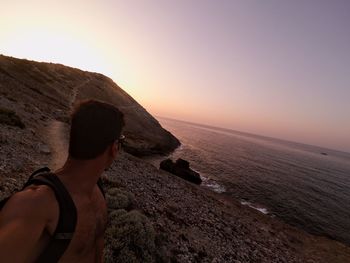 People looking at sea against sky during sunset