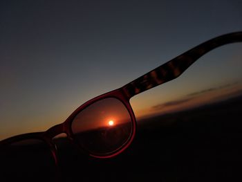 Close-up of sunglasses against sky during sunset