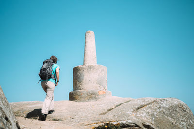 Low angle view of woman walking on rock against clear blue sky