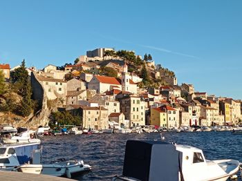 Buildings by sea against clear blue sky