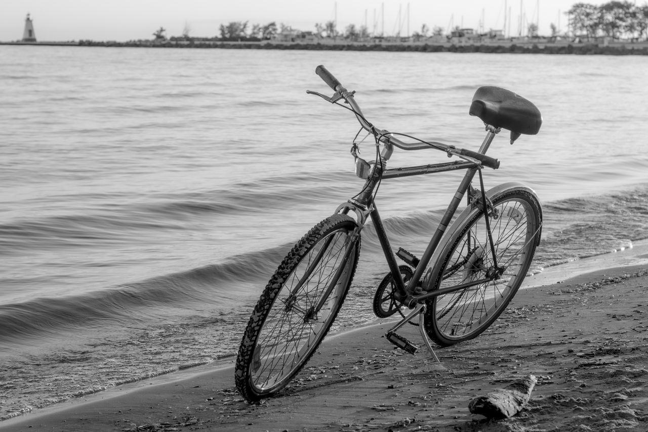 transportation, water, bicycle, mode of transportation, vehicle, beach, nature, land, black and white, sea, land vehicle, sky, day, no people, monochrome, road bicycle, sports equipment, travel, monochrome photography, sand, outdoors, tranquility, activity, cycling, beauty in nature, scenics - nature, bicycle wheel, city, sports, tranquil scene, environment