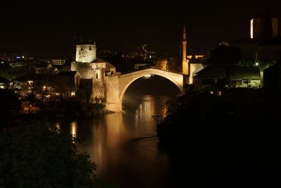 Arch bridge over river against buildings at night