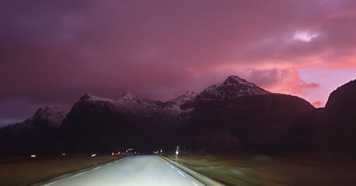 Road amidst illuminated mountains against sky at sunset