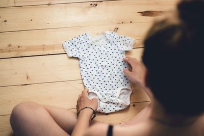 High angle view of woman with baby clothing sitting on hardwood floor