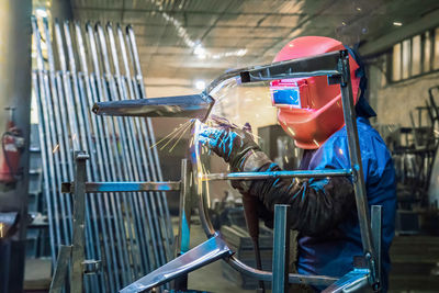 Welder in production is engaged in the manufacture of products. in a mask, in gloves, sparks fly