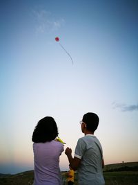 Rear view of couple flying against sky during sunset