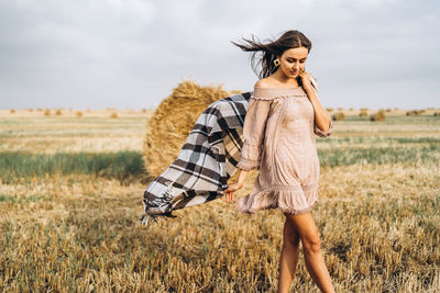 Smiling woman in sunglasses with bare shoulders on a background of wheat field and bales of hay.