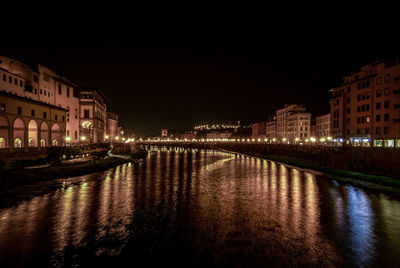 Illuminated buildings by river against sky at night