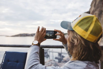 Rear view of person photographing with mobile phone against sky
