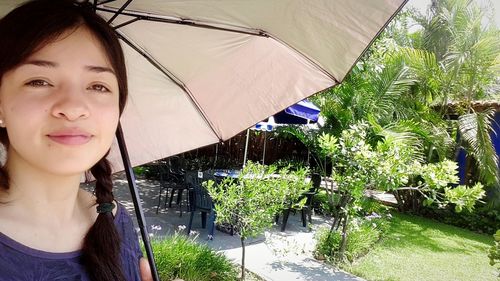 Smiling young woman by plants against trees
