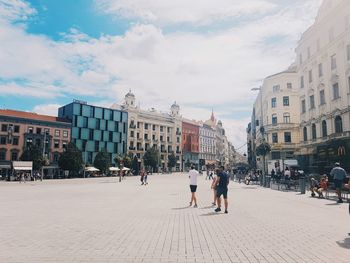 People walking on street amidst buildings in city against sky
