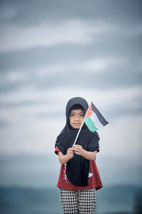 Portrait of young woman holding umbrella against sky