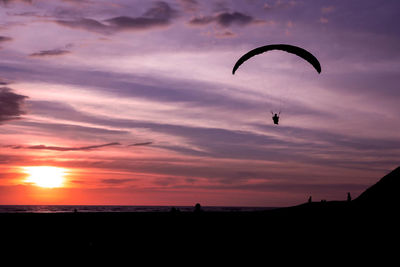 Silhouette person flying over sea against romantic sky